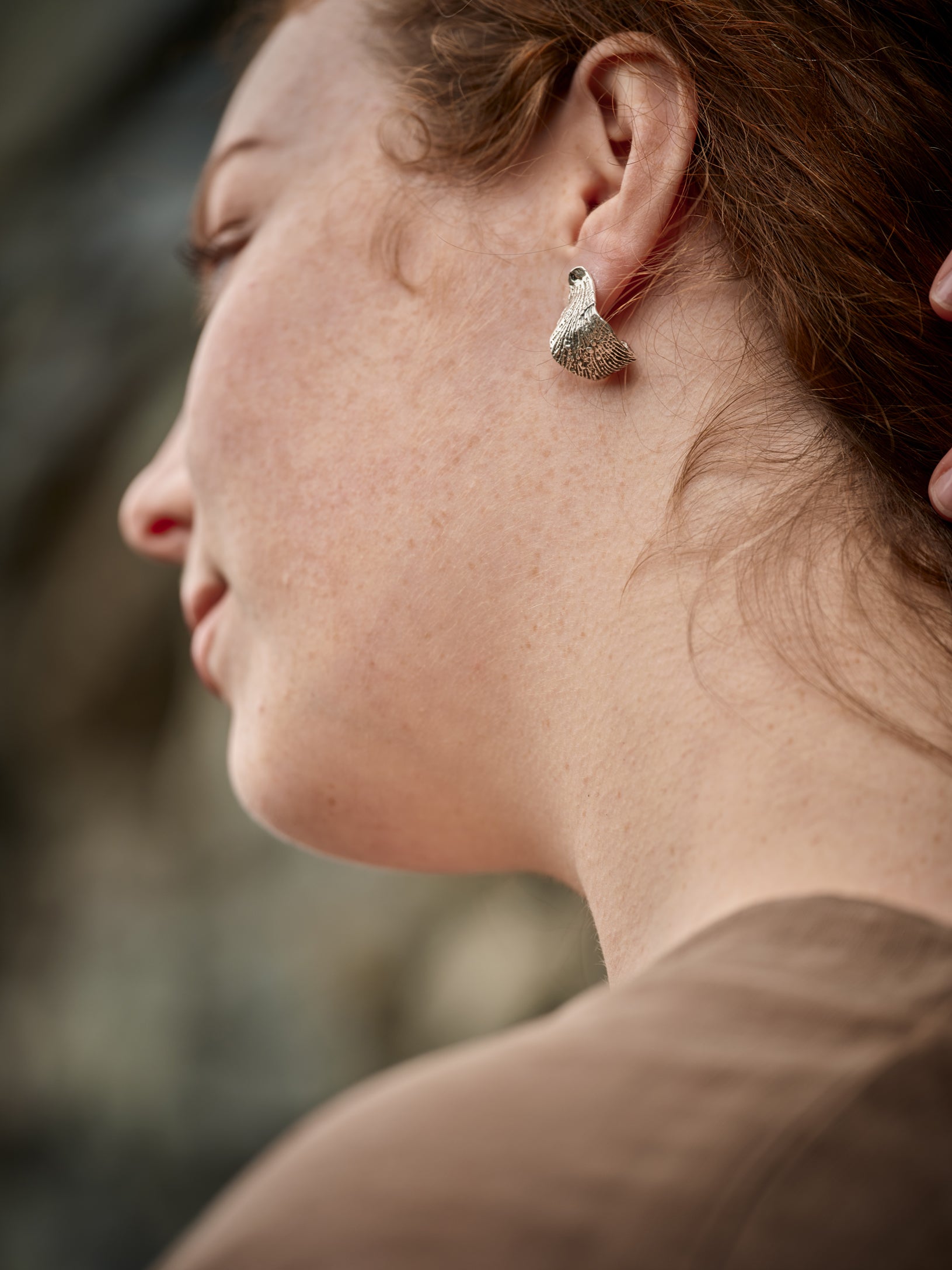 Femme se tenant les cheveux pour laisser apparaître  une boucle d'oreille en argent texturée