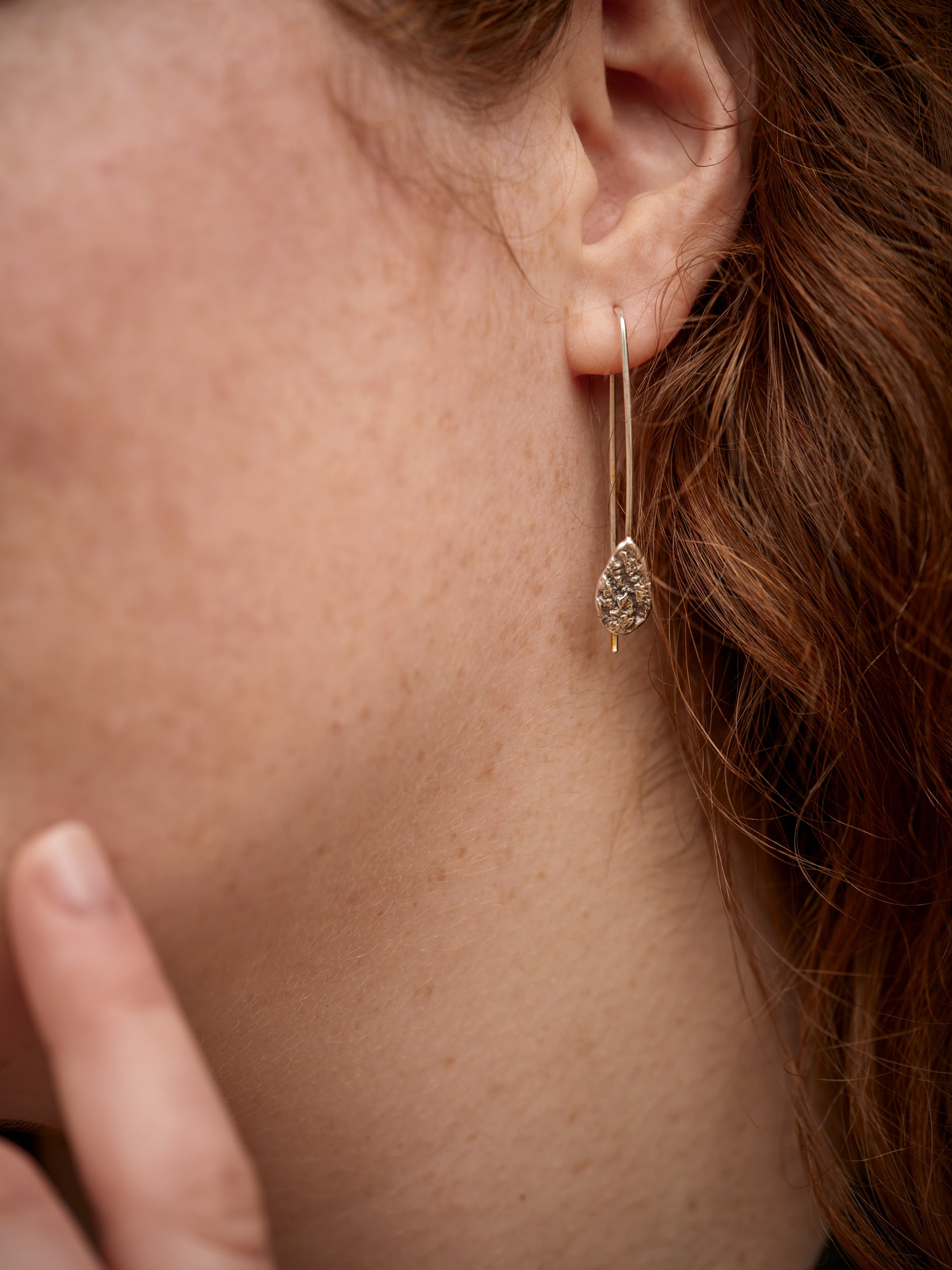 Gros plan d'une oreille portant un crochet d'oreille en argent texturé en forme de goutte